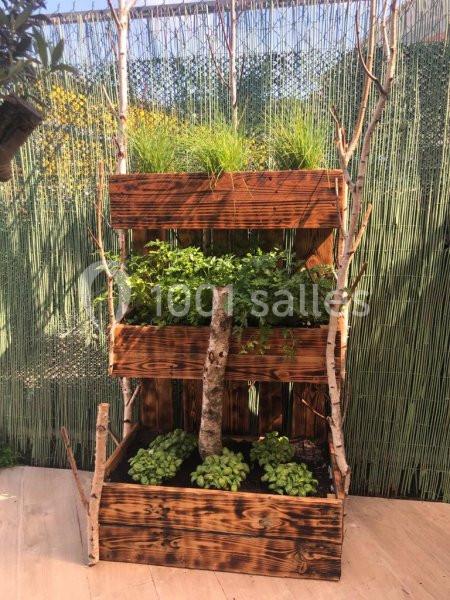 Jardinière verticale en bois avec plusieurs niveaux, contenant des herbes aromatiques et entourée de branches décoratives.
