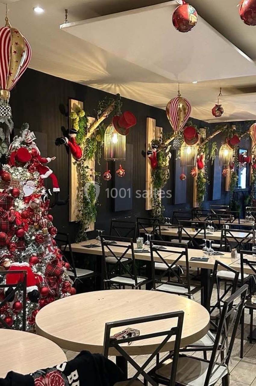 Salle de restaurant décorée pour Noël avec un sapin rouge et argent, des guirlandes et des suspensions festives.