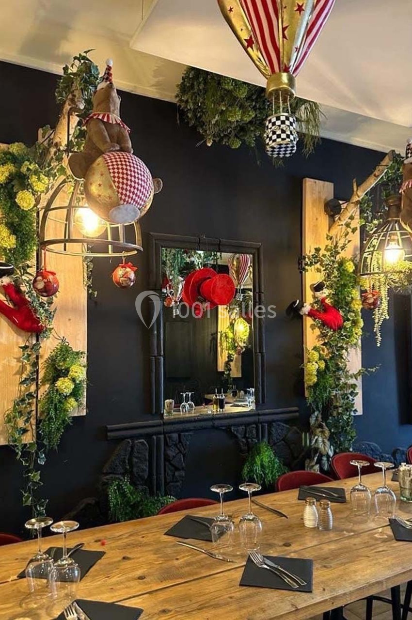 Salle à manger décorée avec des éléments festifs, des plantes suspendues et des luminaires originaux au-dessus d'une grande…