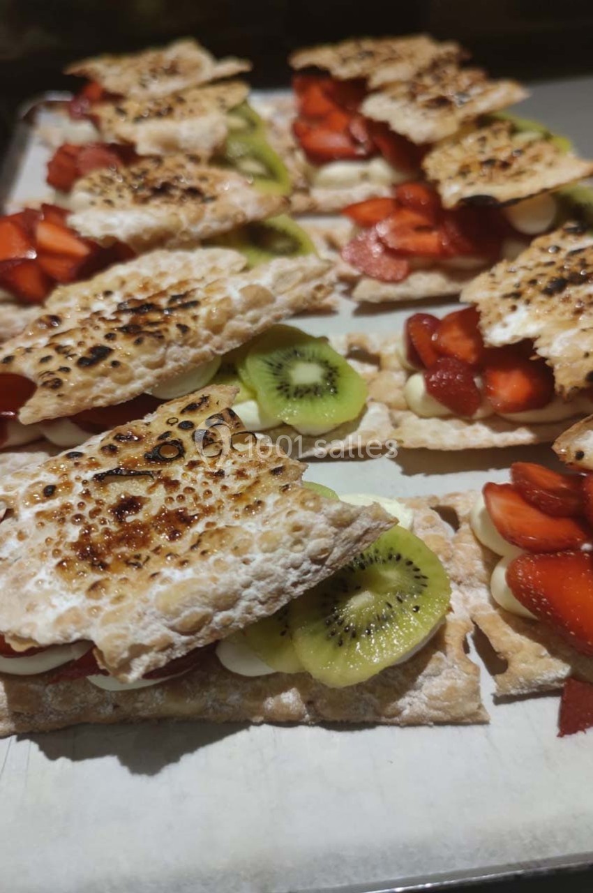 Dessert composé de morceaux de pâte croustillante garnis de fraises, de kiwis et de crème, disposés sur une plaque.
