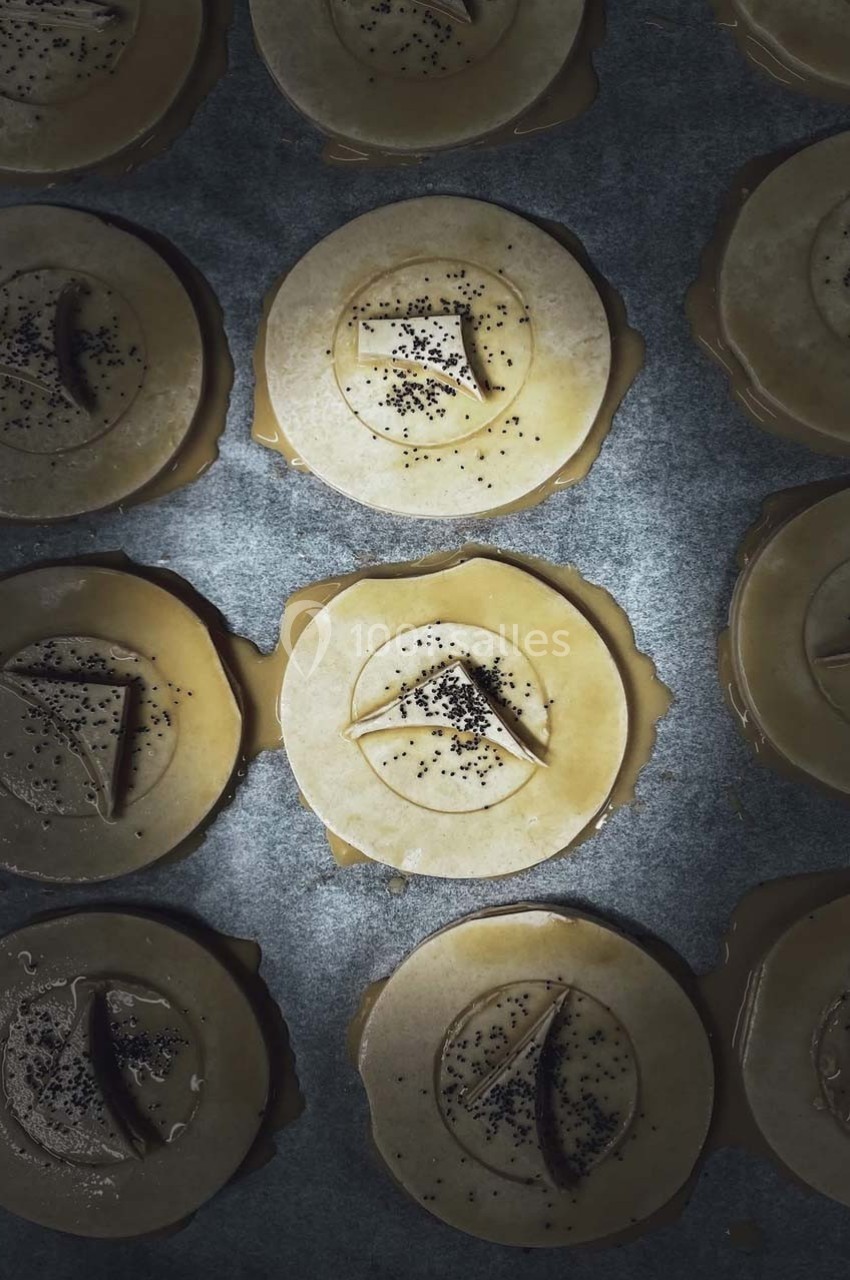 Pâtisseries rondes crues garnies de graines de pavot et de décorations en pâte, disposées sur une plaque sombre.