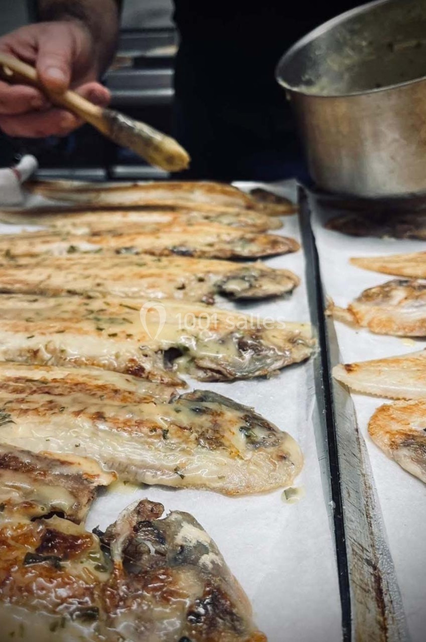 Filets de poisson grillés alignés sur du papier cuisson, avec une main appliquant une sauce à l'aide d'un pinceau.