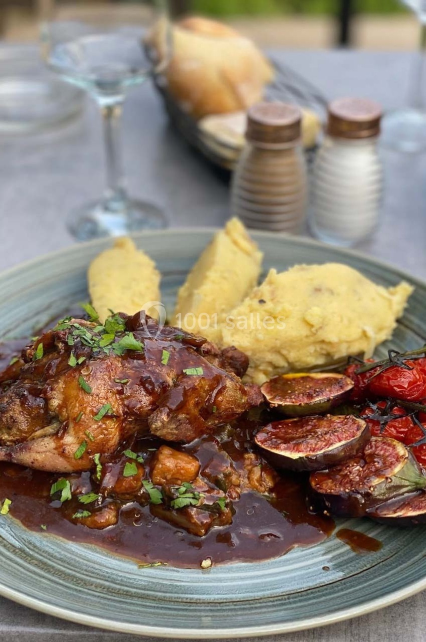 Assiette contenant du poulet en sauce, figues rôties, tomates grillées et purée, servie sur une table dressée.