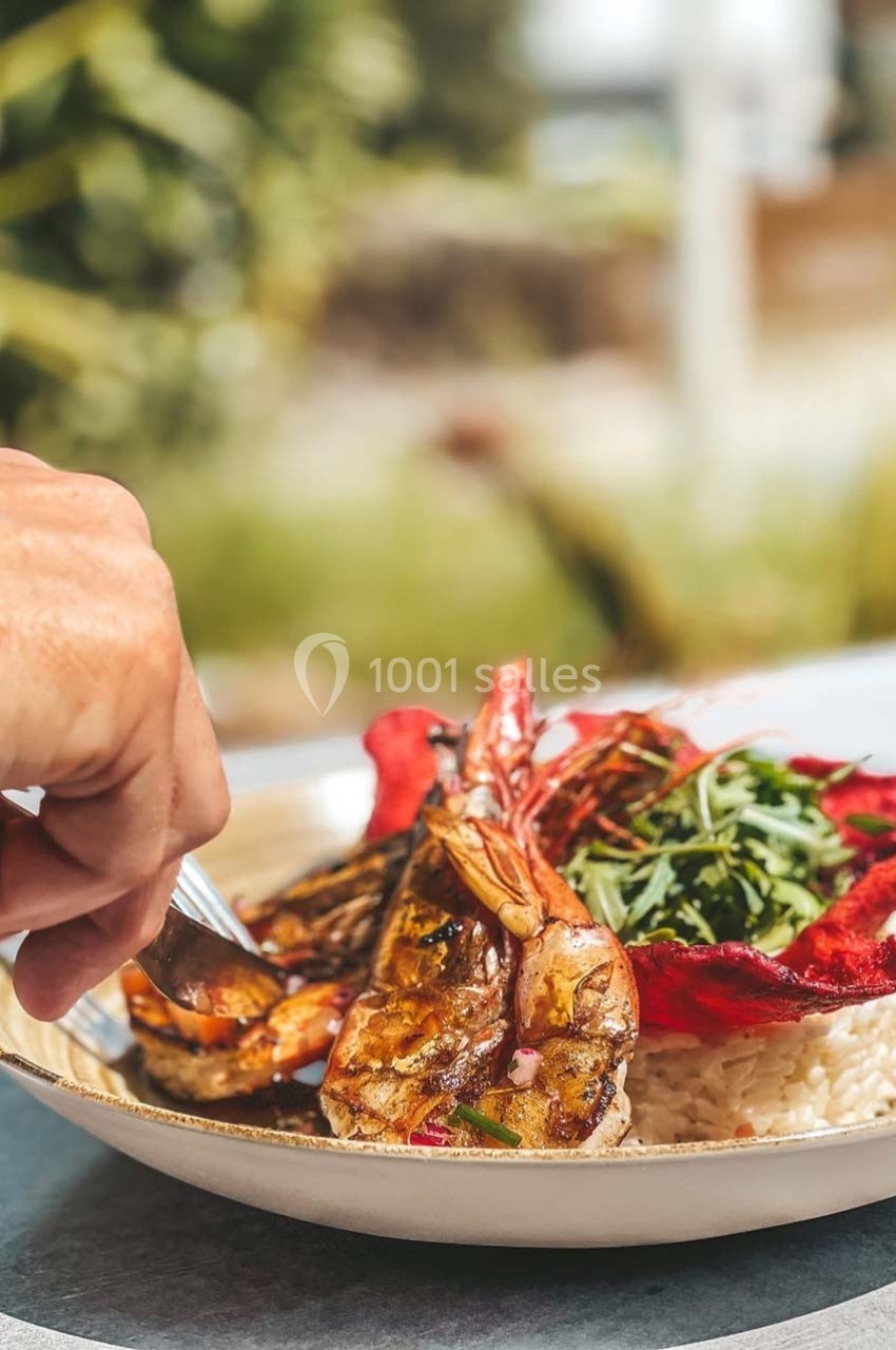 Assiette de crevettes grillées servies avec du riz, des légumes et des chips de betterave, dégustée en extérieur.