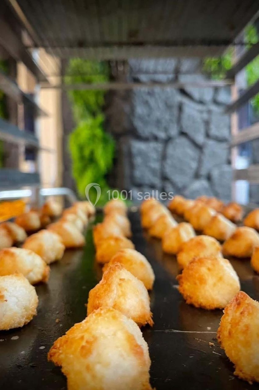 Petits biscuits dorés alignés sur une plaque de cuisson, avec un arrière-plan flou de verdure et de pierre.