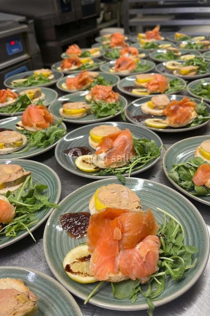 Assiettes garnies de saumon fumé, foie gras, citron, roquette et sauce, disposées sur un plan de travail en cuisine.