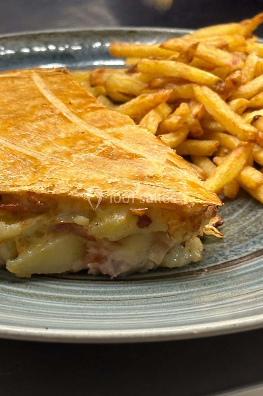 Part de tourte dorée au fromage et jambon servie avec des frites croustillantes sur une assiette.