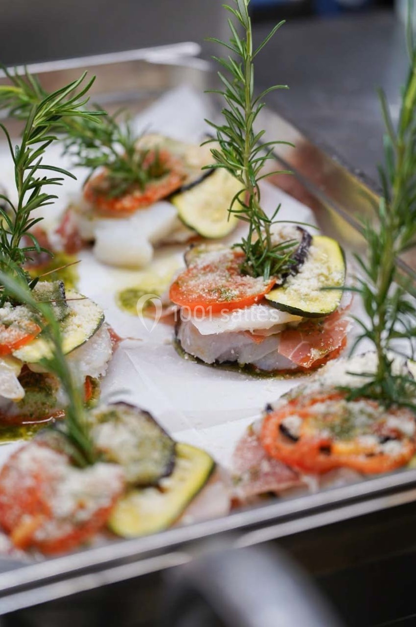 Tranches de légumes grillés, poisson et herbes fraîches disposés en couches sur un plateau de cuisson.