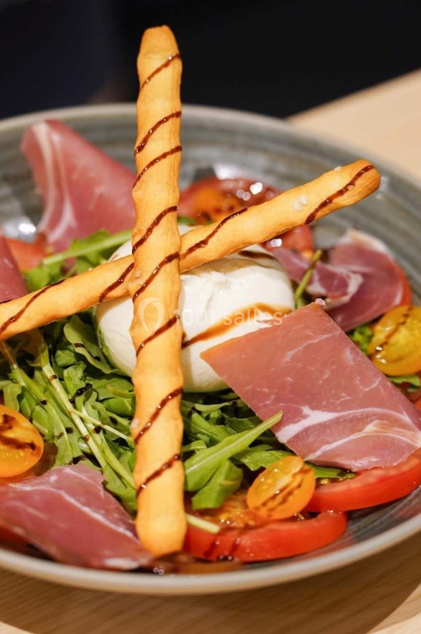 Assiette de salade avec roquette, tomates, burrata, jambon cru, gressins et filet de vinaigre balsamique.