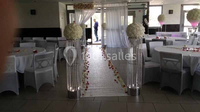 Salle de réception décorée avec des tables rondes, une allée centrale ornée de pétales et colonnes fleuries.