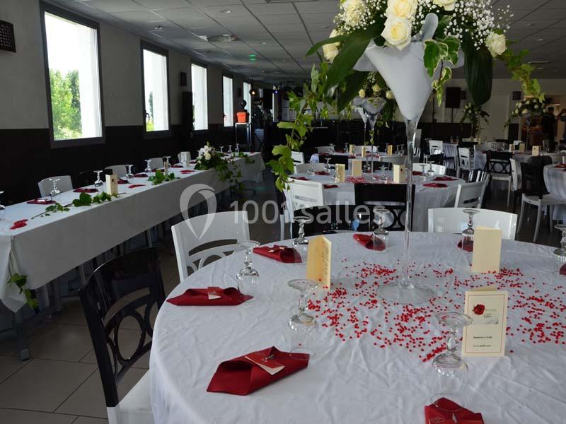 Salle de réception décorée avec des tables blanches, nappes ornées de pétales rouges et centres de table floraux.
