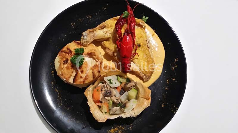 Assiette composée de poulet, écrevisse, légumes en sauce et pain garni, présentée sur une assiette noire.