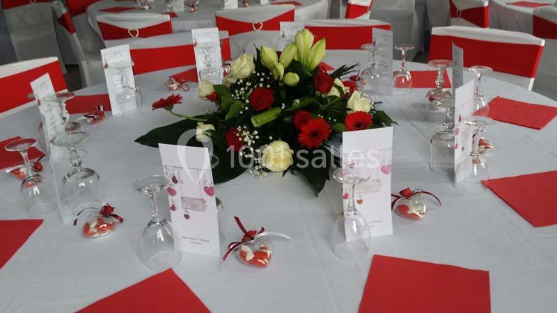 Table décorée pour un événement avec nappes blanches, serviettes rouges, centre de table floral et menus disposés.