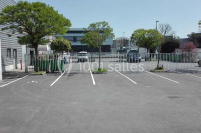 Parking vide avec marquages au sol, entouré de bâtiments industriels et d'arbres sous un ciel dégagé.