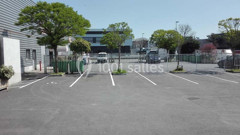 Parking vide avec marquages au sol, entouré de bâtiments industriels et d'arbres sous un ciel dégagé.