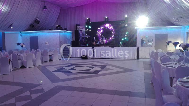 Salle de réception décorée avec des tables dressées, des chaises blanches et une scène éclairée pour un événement.