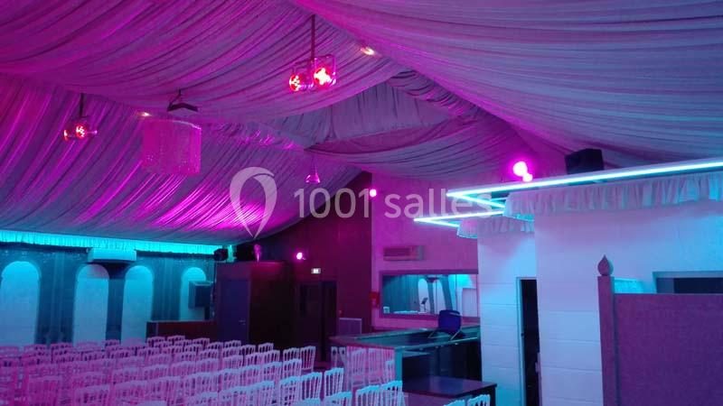 Salle décorée avec un éclairage rose et bleu, des chaises blanches alignées et un plafond drapé.