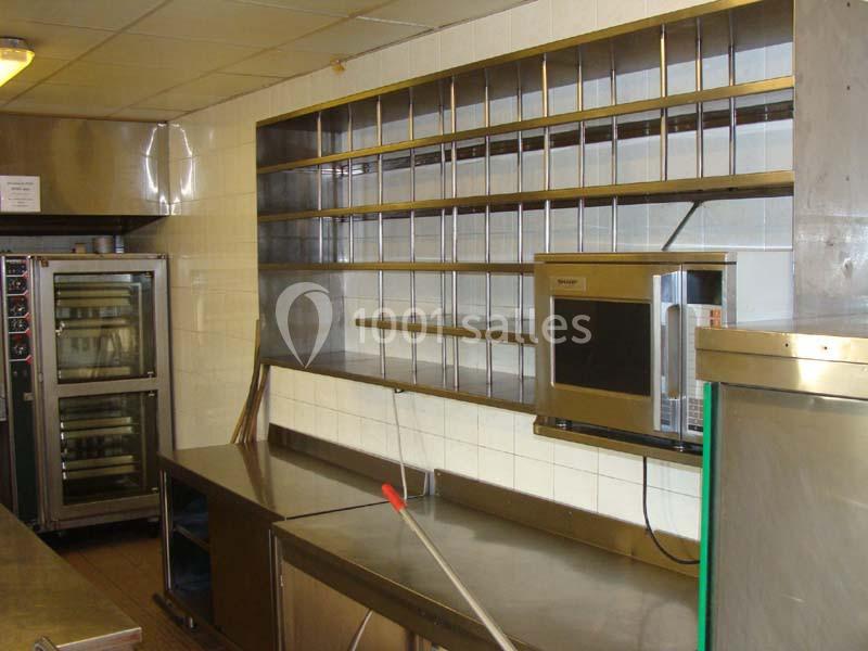 Cuisine professionnelle avec étagères métalliques vides, four encastré et plan de travail en acier inoxydable.