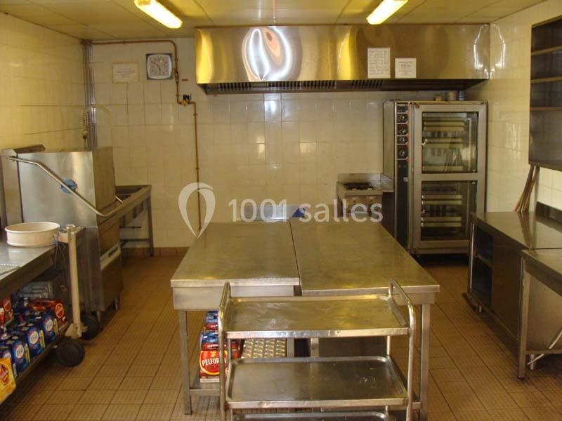 Cuisine professionnelle avec plans de travail en inox, four, étagères et équipements de restauration.