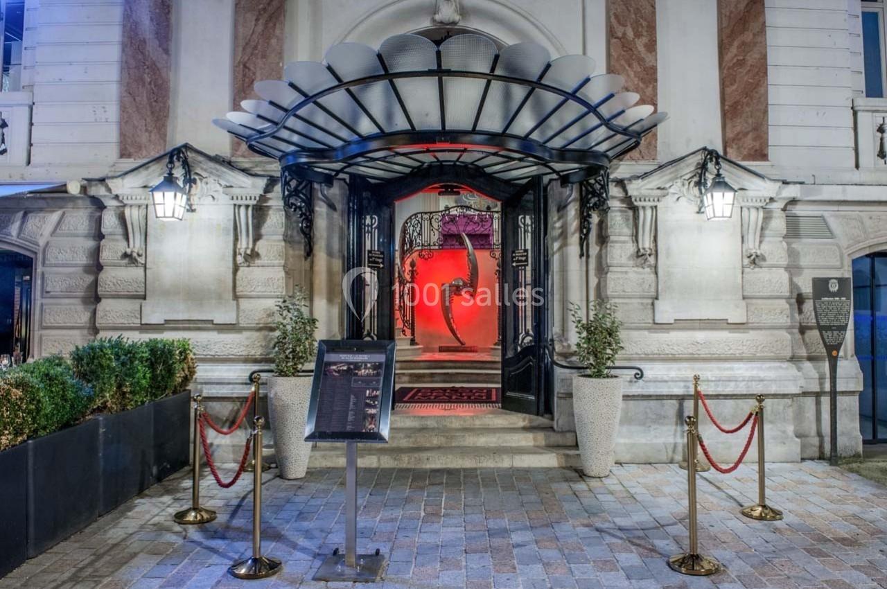Entrée d'un bâtiment élégant avec porte ouverte, tapis rouge, éclairage rouge et cordons de sécurité.