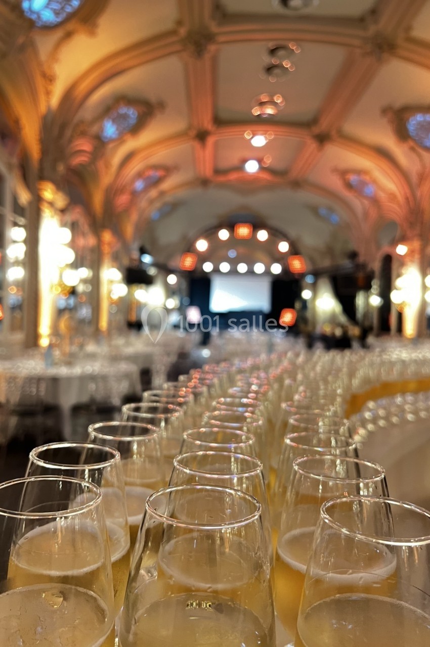 Rangée de verres de champagne alignés sur une table dans une salle élégante avec un plafond voûté éclairé.
