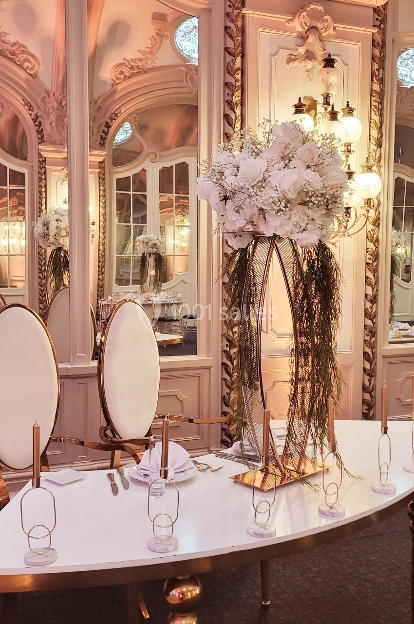 Table élégante décorée de fleurs blanches et de bougies dorées dans une salle au style classique avec miroirs ornés.