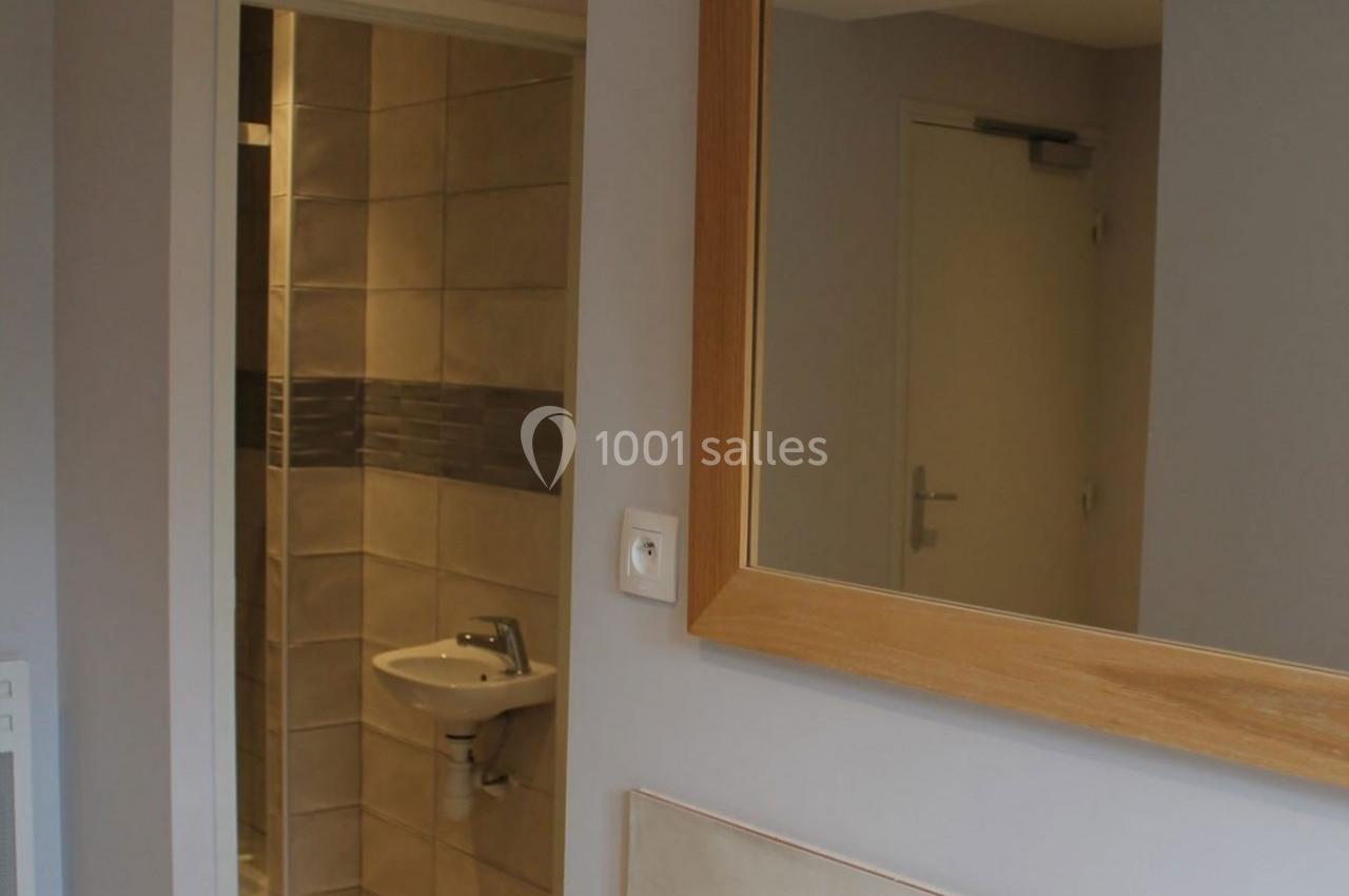 Vue d'une salle de bain avec un lavabo, un miroir encadré en bois et des carreaux beige et gris.