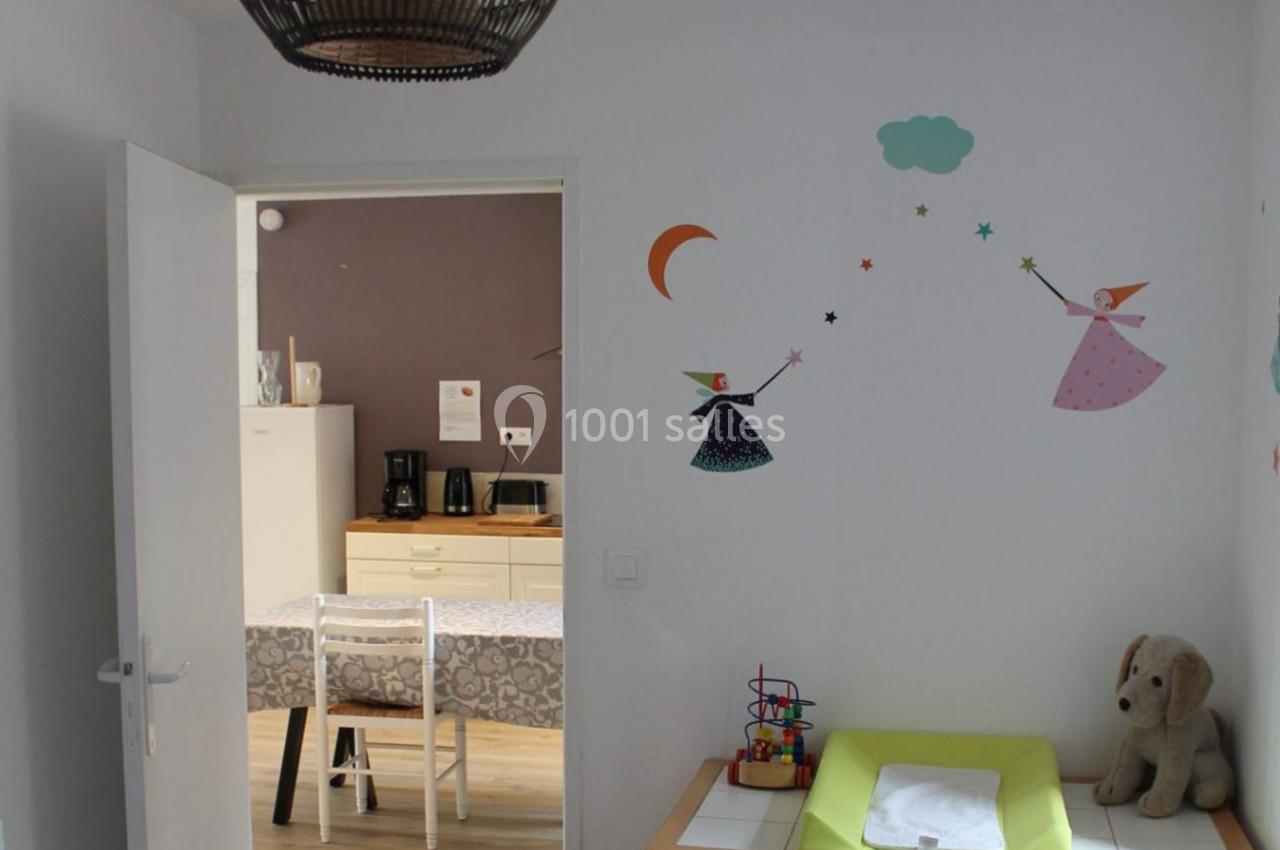 Vue d'une chambre d'enfant avec table à langer, décorations murales colorées et aperçu d'une cuisine en arrière-plan.