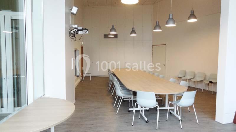 Salle de réunion lumineuse avec une grande table ovale entourée de chaises et des lampes suspendues au plafond.