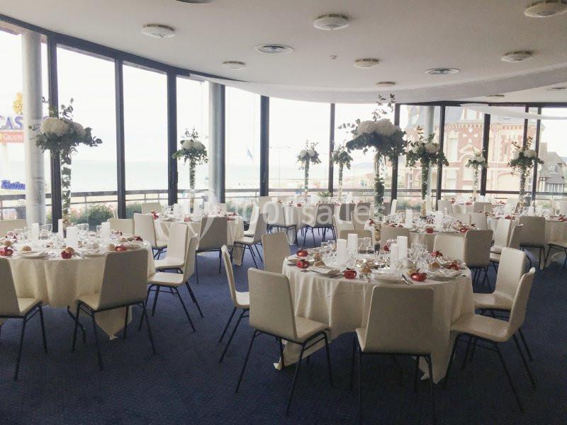 Location salle Villers-sur-Mer (Calvados) - Salle Panoramique Villers Sur Mer #3 Salle de réception lumineuse avec tables rondes dressées, nappes blanches et décorations florales, vue sur l'extérieur.