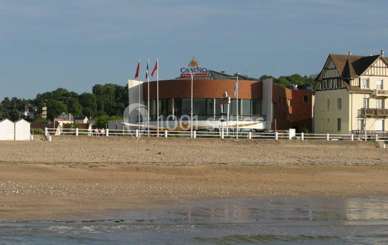 Bâtiment moderne d'un casino en bord de plage, entouré de maisons et de verdure, avec des drapeaux sur le toit.