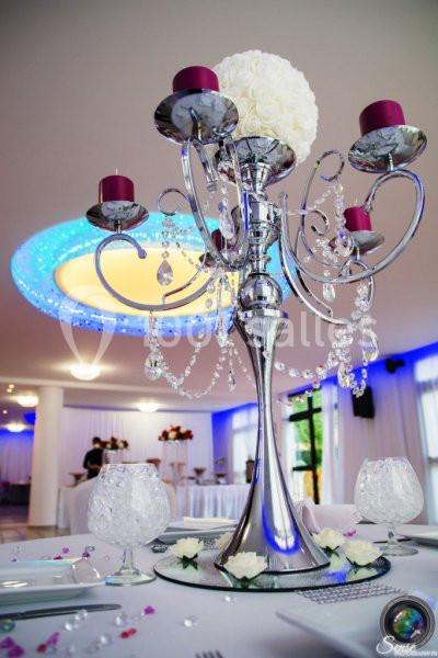 Chandelier argenté orné de bougies rouges et de cristaux, décoré de fleurs blanches, sur une table de réception élégante.