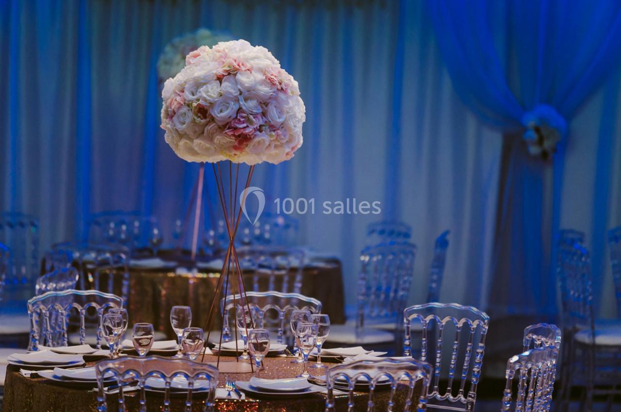 Centre de table floral avec des roses blanches et roses, entouré de chaises transparentes dans une salle décorée.