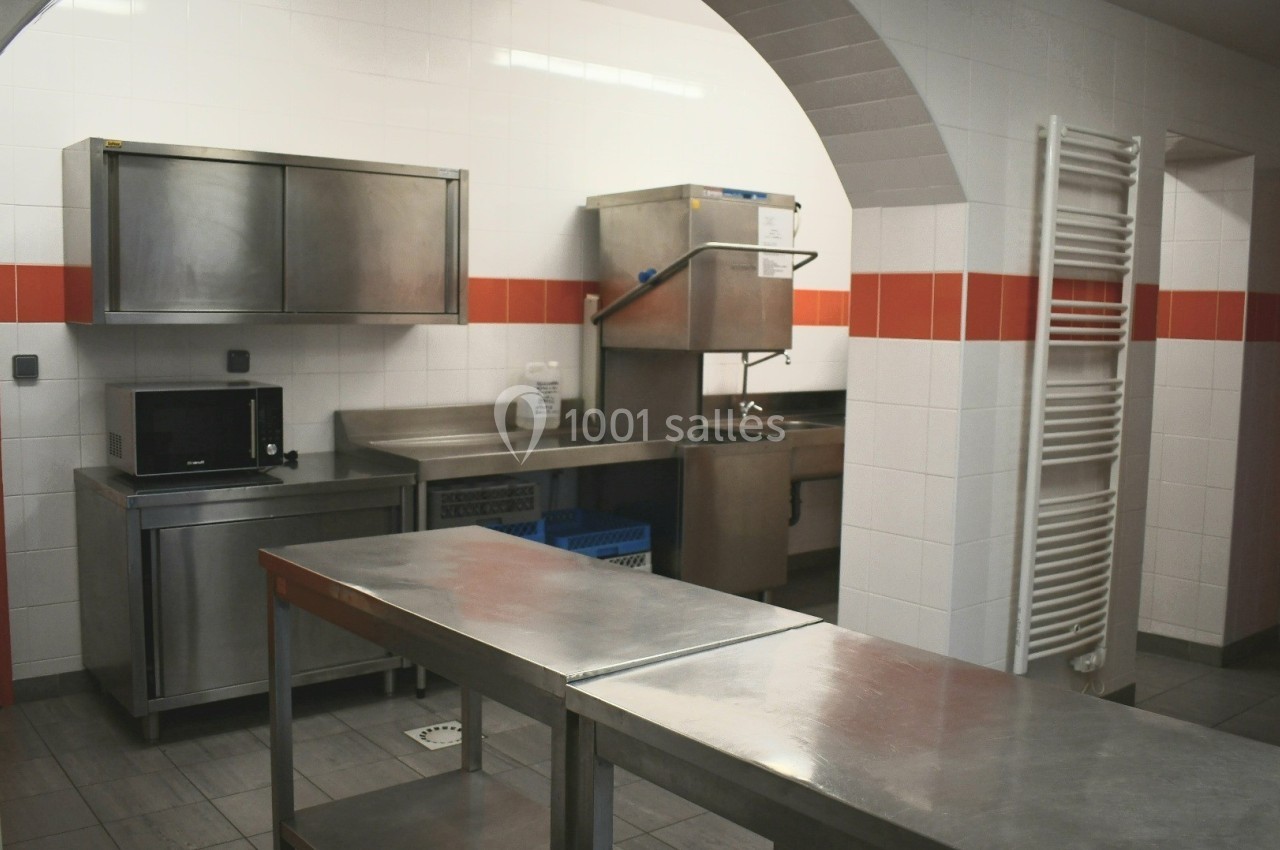 Cuisine professionnelle avec plans de travail en inox, évier, micro-ondes et étagères murales dans un espace carrelé.