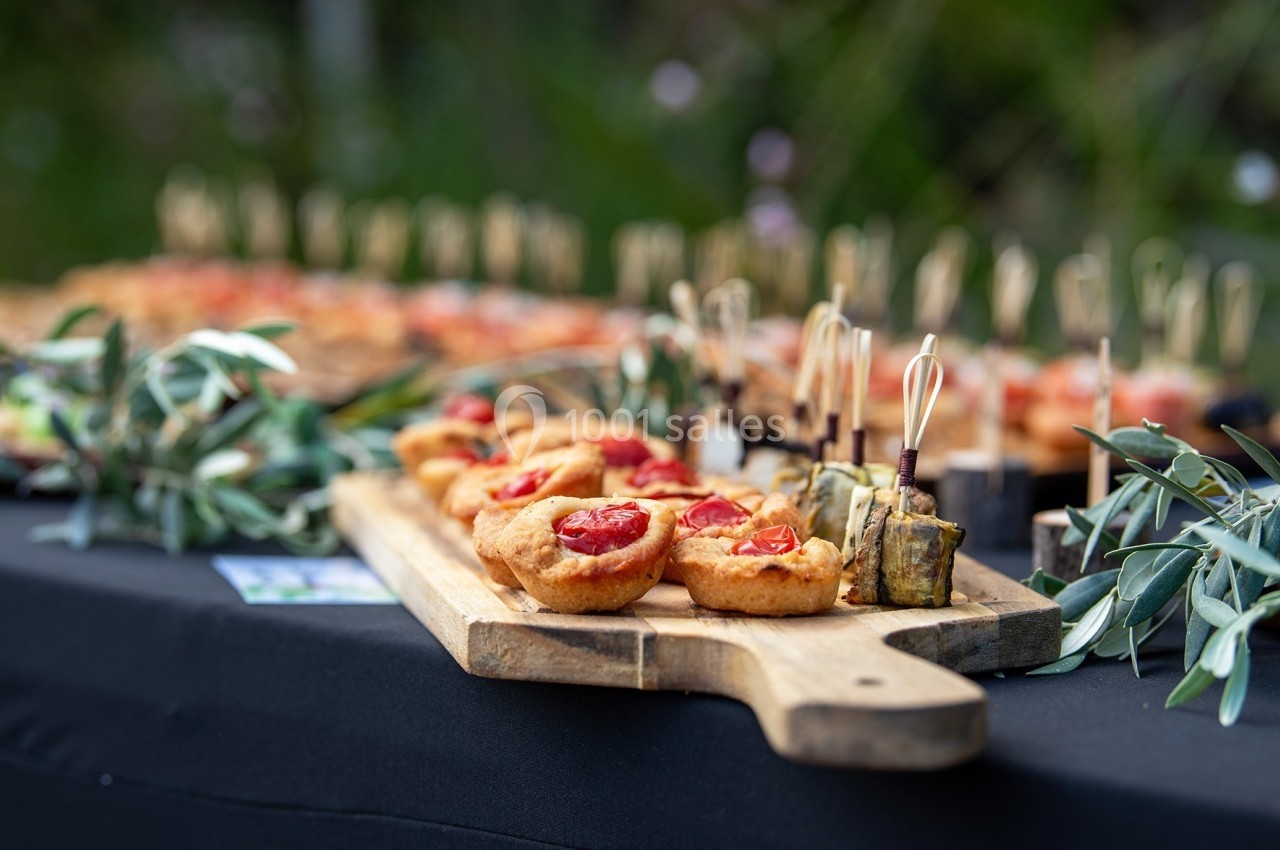 Plateau en bois avec amuse-bouches, dont des tartelettes aux tomates et des bouchées végétales, sur une nappe noire.
