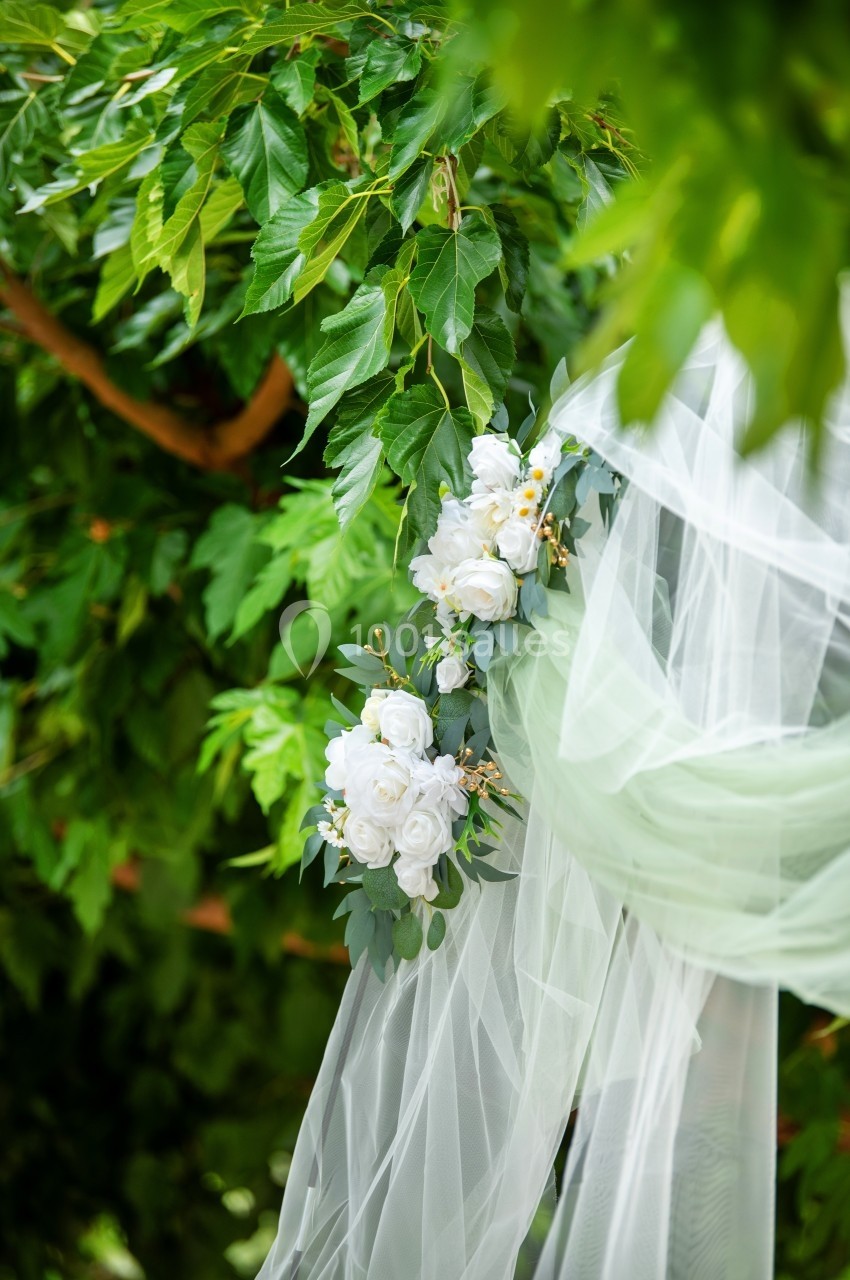 Voile blanc décoré de fleurs blanches suspendu à une branche d'arbre feuillu.
