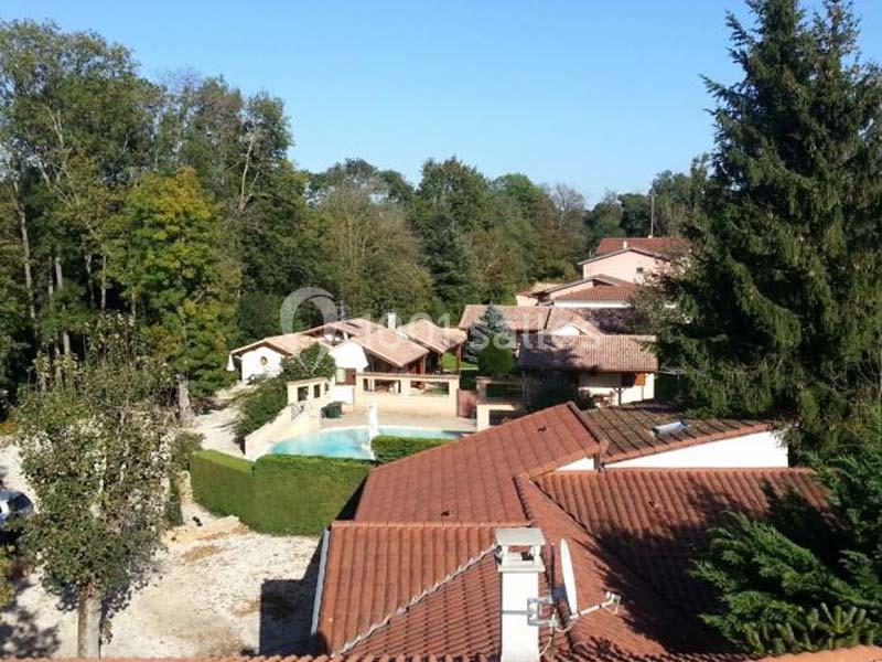 Location salle Saint-Georges-d'Espéranche (Isère) - Les Jardins du Castel #17 Vue aérienne d'un ensemble de maisons avec toits en tuiles rouges, entourées d'arbres et d'une piscine au centre.