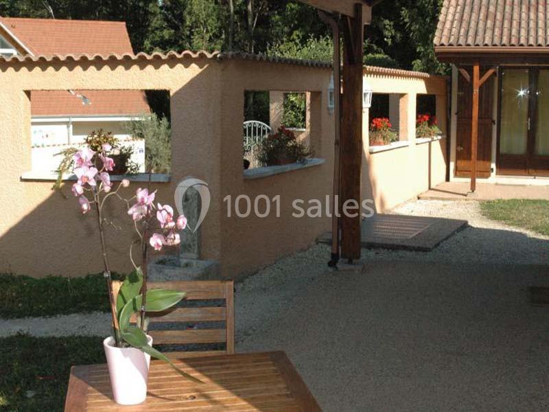 Location salle Saint-Georges-d'Espéranche (Isère) - Les Jardins du Castel #21 Une orchidée rose en pot posée sur une table en bois dans une cour extérieure ensoleillée avec des murs en crépi beige.