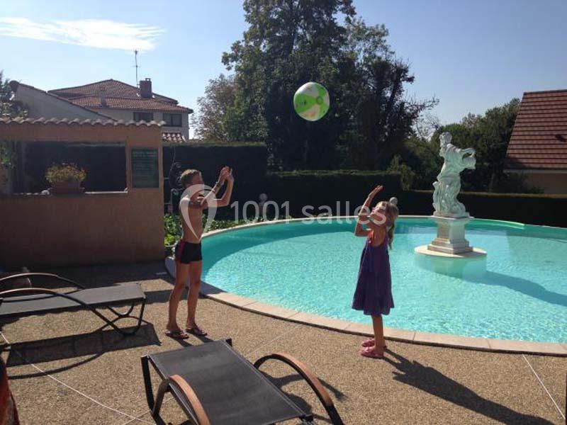 Location salle Saint-Georges-d'Espéranche (Isère) - Les Jardins du Castel #22 Deux enfants jouent avec un ballon près d'une piscine circulaire entourée de chaises longues et d'une statue.