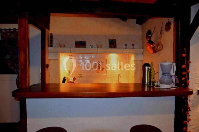 Location salle Saint-Georges-d'Espéranche (Isère) - Les Jardins du Castel #31 Cuisine rustique avec un bar en bois, éclairage chaleureux, cafetière et ustensiles suspendus au mur.