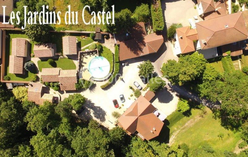 Location salle Saint-Georges-d'Espéranche (Isère) - Les Jardins du Castel #2 Vue aérienne d'un complexe résidentiel entouré de verdure, avec une piscine centrale et des bâtiments en toits rouges.