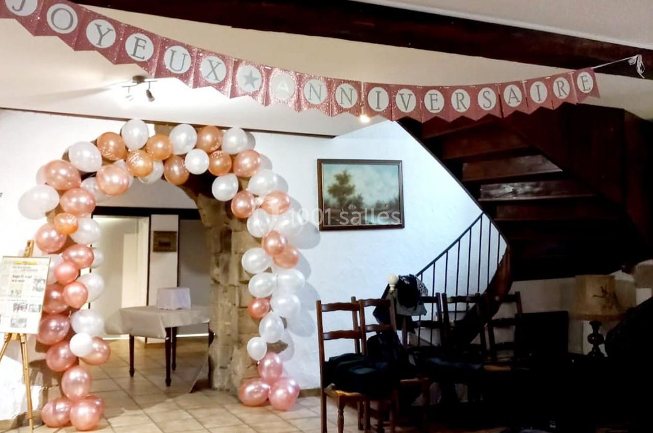 Location salle Saint-Georges-d'Espéranche (Isère) - Les Jardins du Castel #28 Décoration d'anniversaire avec arche de ballons blancs et roses, guirlande ’Joyeux Anniversaire’ et intérieur rustique.