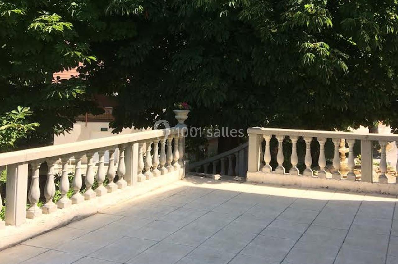 Location salle Saint-Georges-d'Espéranche (Isère) - Les Jardins du Castel #11 Terrasse en pierre bordée de balustrades blanches, entourée de végétation dense et ombragée.