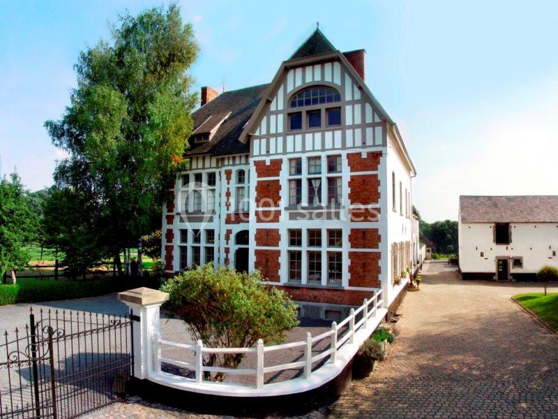 Bâtiment à colombages avec façade en briques rouges, entouré d'une cour pavée et d'arbres.