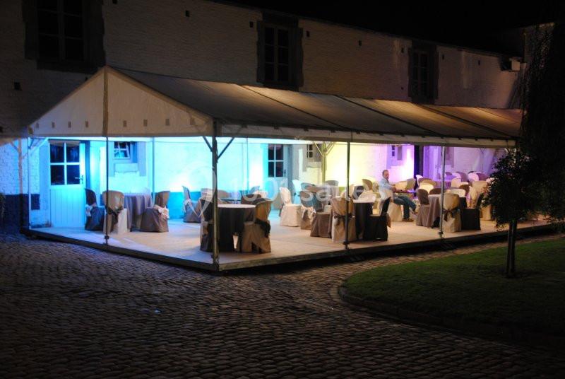 Terrasse couverte éclairée de lumières colorées, aménagée avec des tables et des chaises pour un événement nocturne.