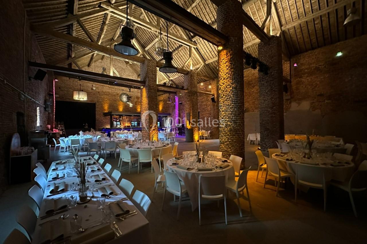 Salle de réception avec tables dressées, éclairage tamisé et murs en briques apparentes.