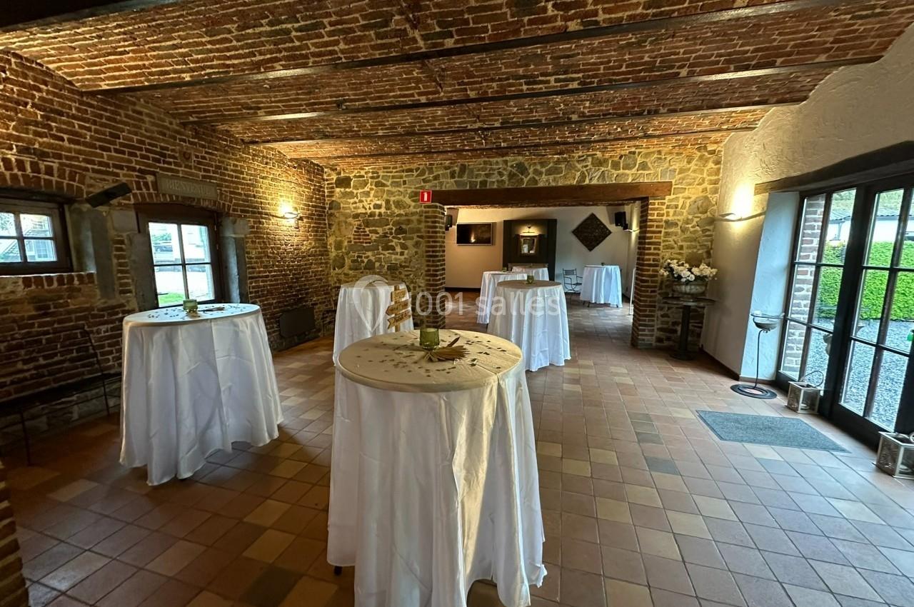 Salle en briques avec des tables hautes recouvertes de nappes blanches, éclairée par des fenêtres et des lumières murales.