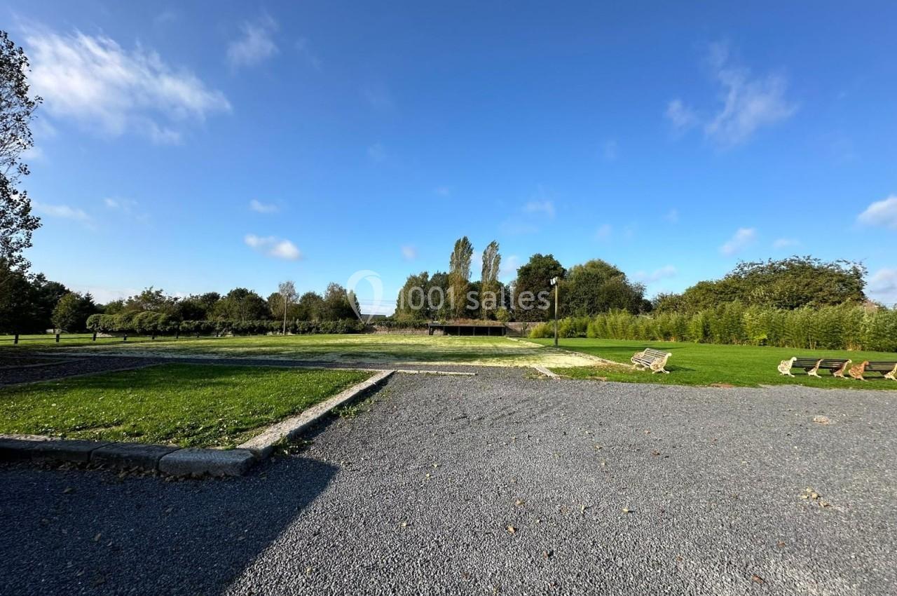 Espace extérieur avec pelouse, allée en gravier, bancs en bois et arbres sous un ciel bleu dégagé.