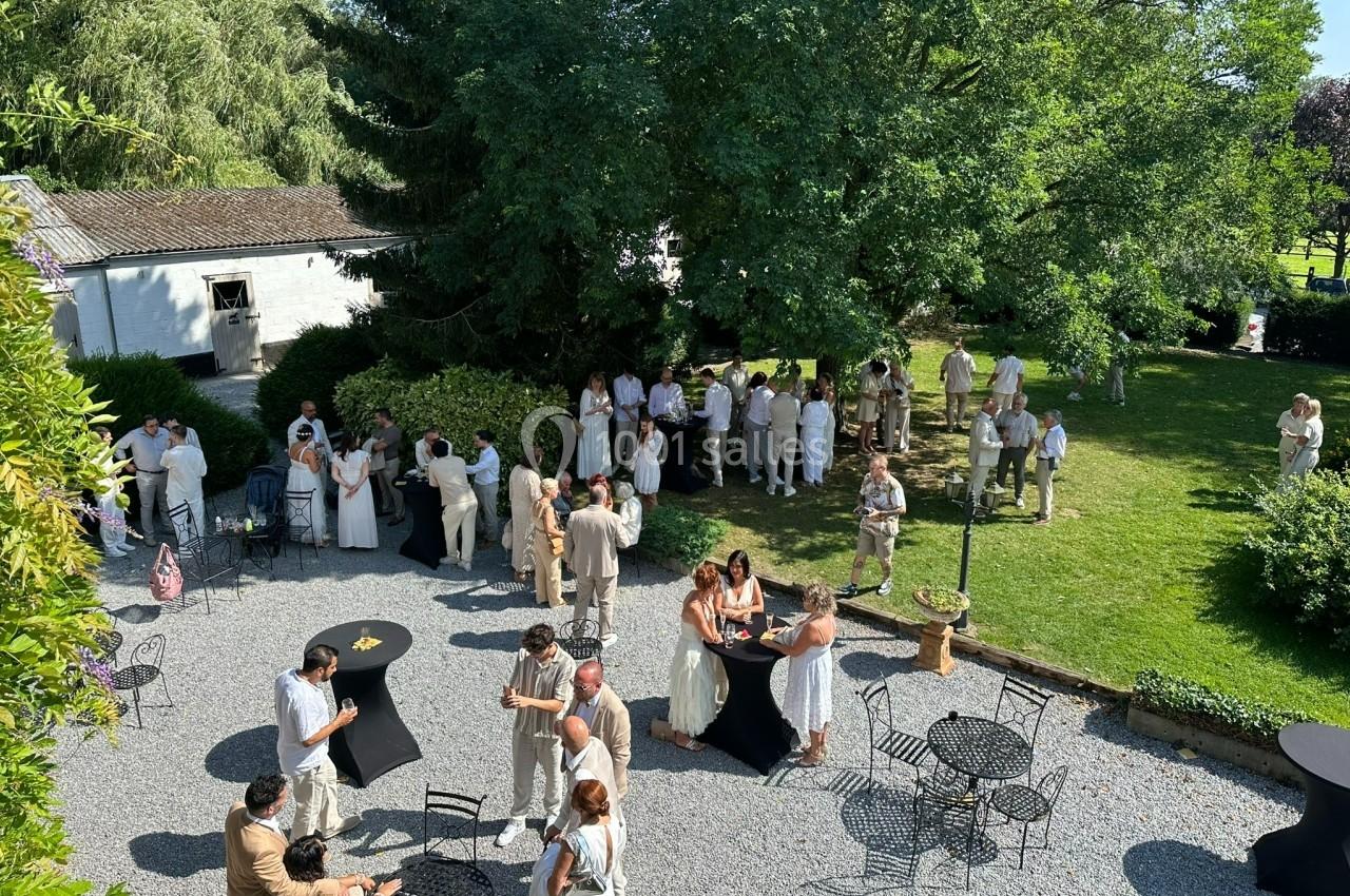Groupe de personnes en tenue claire réunies dans un jardin avec tables et chaises, par une journée ensoleillée.
