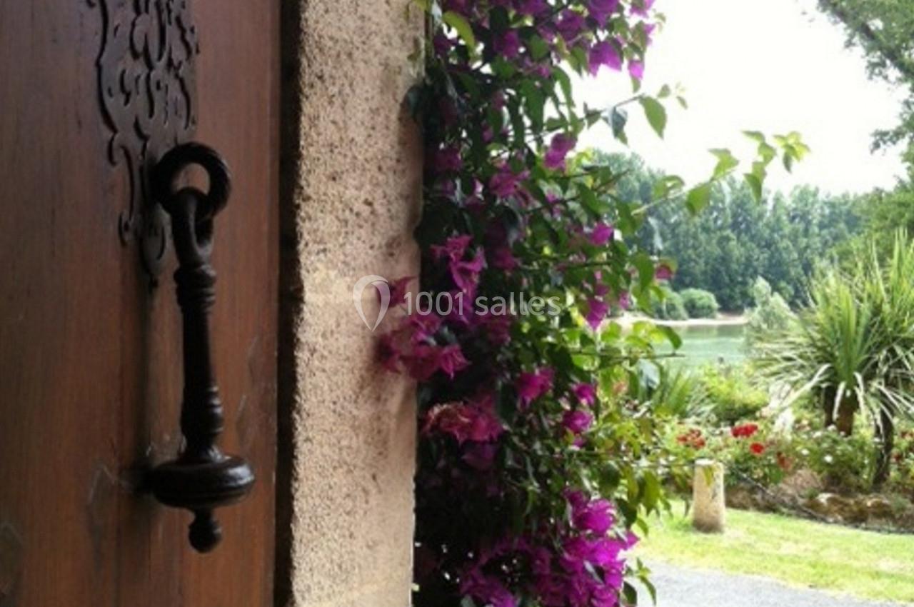 Plante grimpante à fleurs violettes ornant un mur en pierre près d'une porte en bois avec vue sur un jardin.